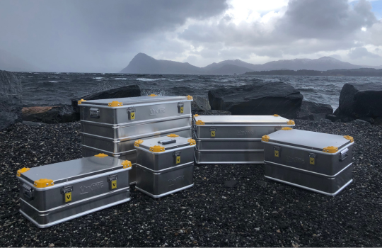 Viking aluminium transportkisten met gele hoeken opgesteld op een rotsachtige kustlijn, met zee en bergachtig landschap op de achtergrond.
