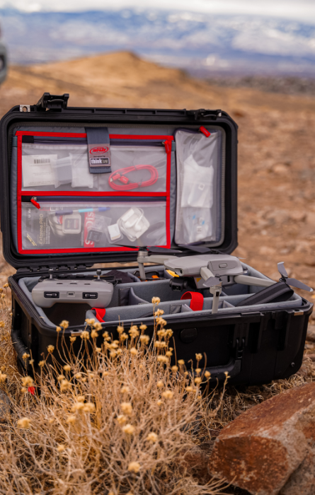 Open zwarte SKB koffer met georganiseerde compartimenten en accessoires, gebruikt voor het veilig opbergen en transporteren van een drone en bijbehorende apparatuur in een buitenomgeving.
