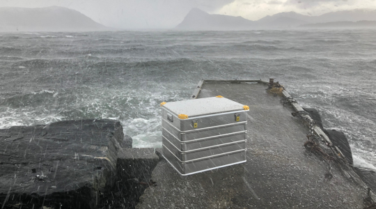 Spatwaterdichte Viking aluminium koffer geplaatst op een pier aan zee tijdens zware regen en ruwe weersomstandigheden.